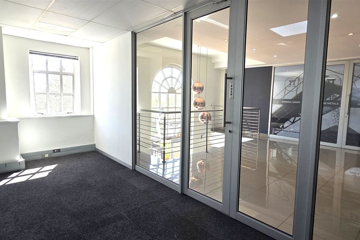 A bright, modern office space featuring glass partitions, tiled and carpeted flooring, and recessed lighting, offering a professional and clean work environment.