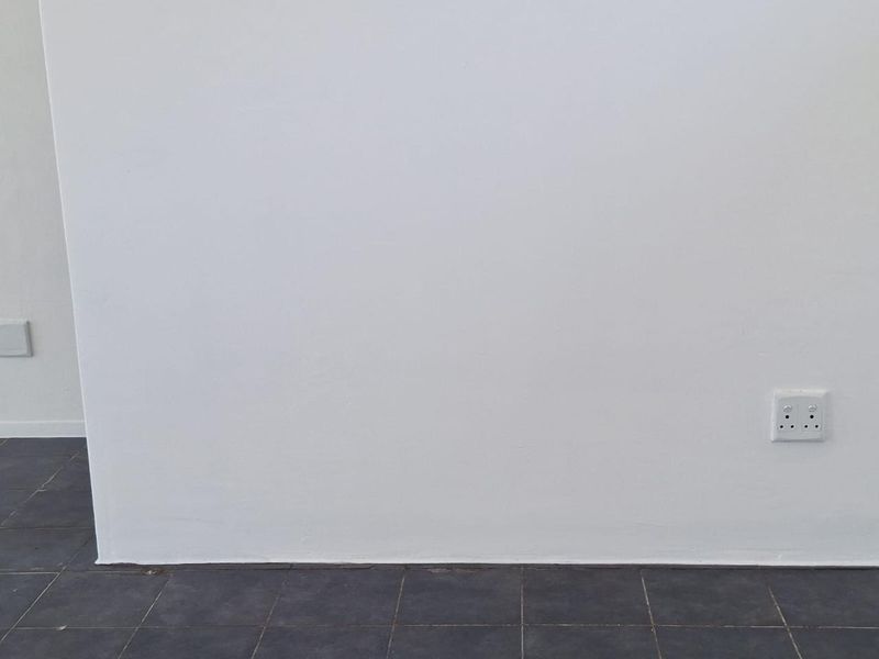 A plain interior wall featuring dark floor tiles and standard electrical power outlets.
