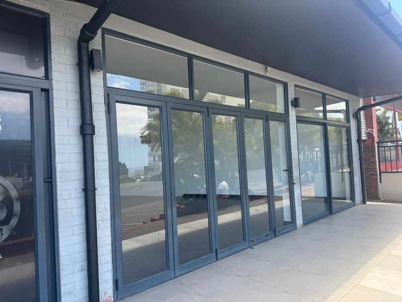 Modern retail storefront featuring large glass bi-fold doors, white painted brick facade, and tiled outdoor walkway.