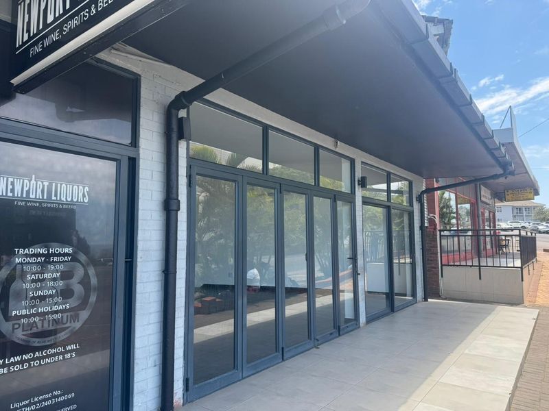 Front facade of a retail storefront featuring large glass folding doors, a covered tiled walkway, and painted brick exterior.
