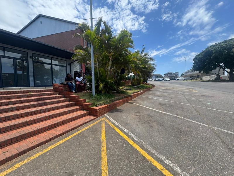 Exterior view of a retail property featuring a brick staircase entrance, paved parking area, and established landscaping.