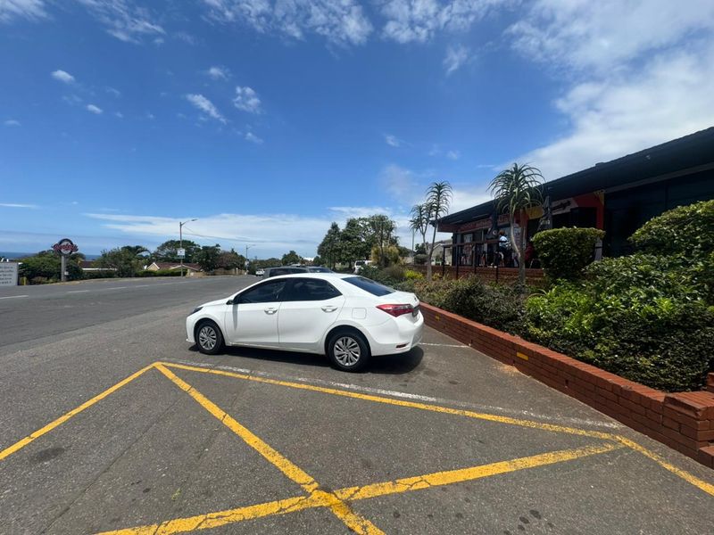 Exterior view of the retail property frontage featuring a paved parking area, brick retaining wall, and landscaped garden beds.