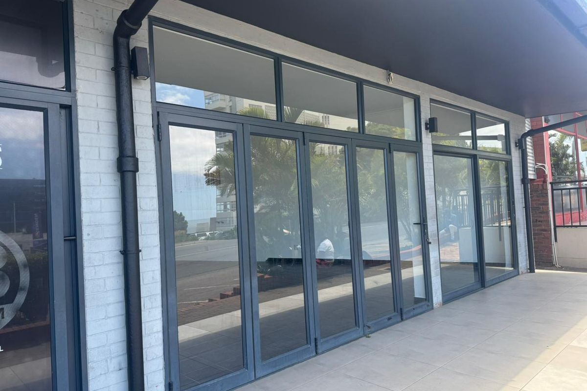 Modern retail storefront featuring large glass bi-fold doors, white painted brick facade, and tiled outdoor walkway.