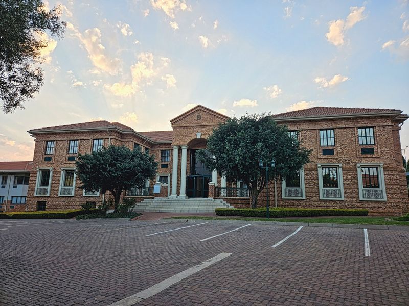A professional exterior view of a multi-story brick office building featuring a grand entrance with columns and a paved parking area.