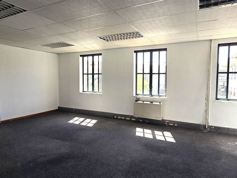 A vacant, open-plan office space featuring a suspended ceiling, recessed lighting, metal-framed windows, and an integrated HVAC unit.