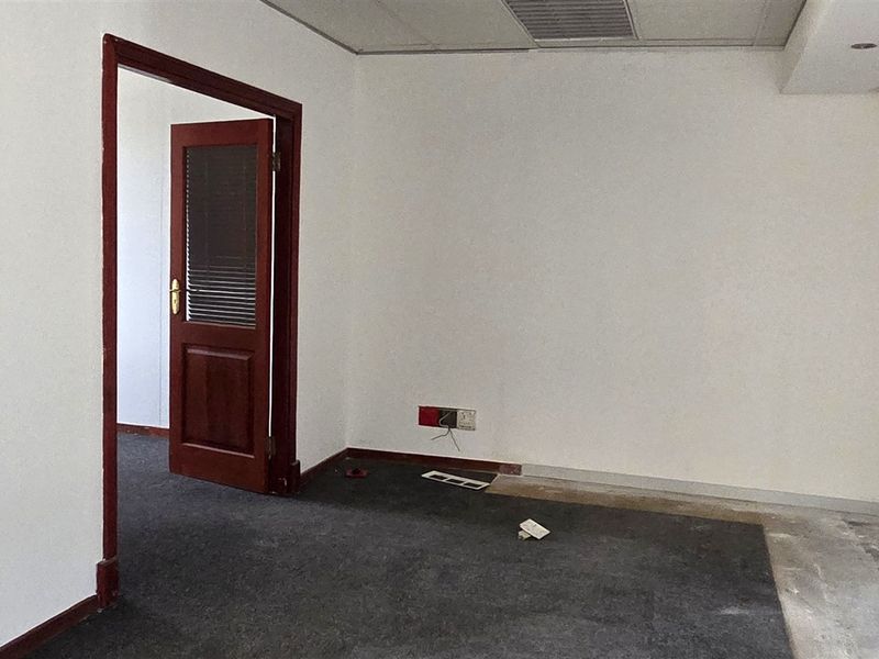 An empty office space featuring a suspended ceiling, air conditioning vent, and timber door frame, currently requiring flooring and wall finish repairs.