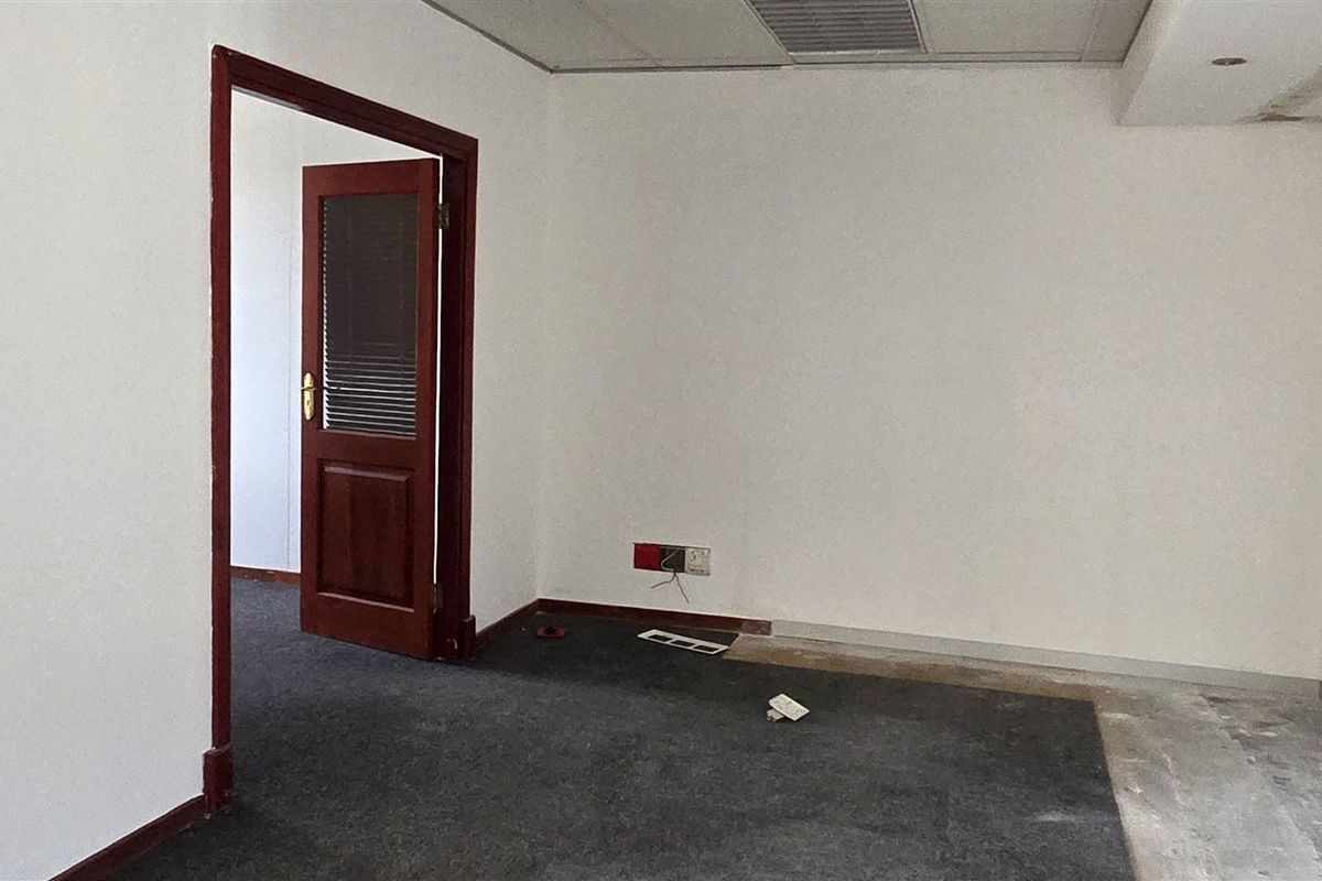 An empty office space featuring a suspended ceiling, air conditioning vent, and timber door frame, currently requiring flooring and wall finish repairs.
