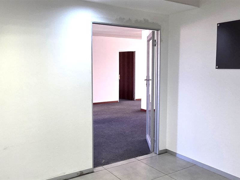 An empty office space featuring tiled flooring in the entrance area, carpeted flooring in the inner room, and a glass door entry.