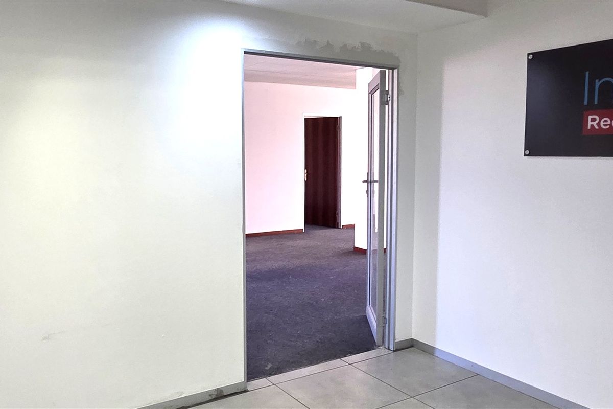 An empty office space featuring tiled flooring in the entrance area, carpeted flooring in the inner room, and a glass door entry.