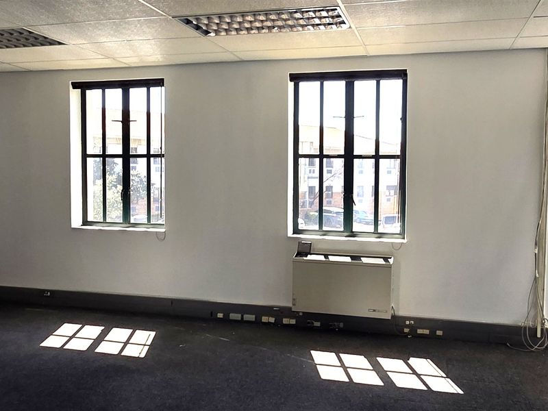 An empty office space featuring a suspended ceiling, recessed lighting, metal-framed windows, and an integrated HVAC unit with carpet flooring.