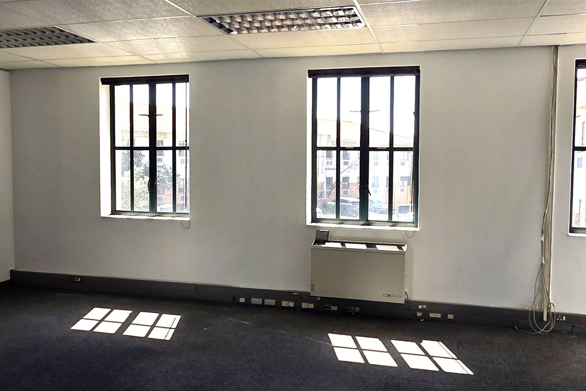 An empty office space featuring a suspended ceiling, recessed lighting, metal-framed windows, and an integrated HVAC unit with carpet flooring.