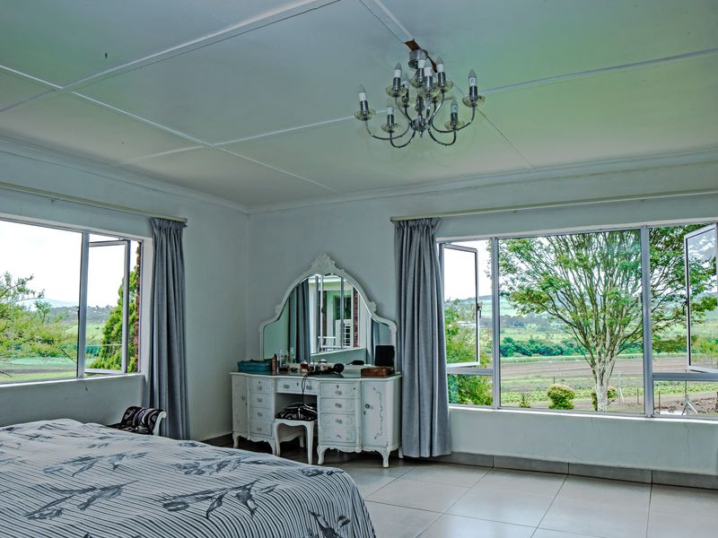 Spacious bedroom featuring large windows with scenic rural views, tiled flooring, and a central chandelier, offering a bright and airy atmosphere.