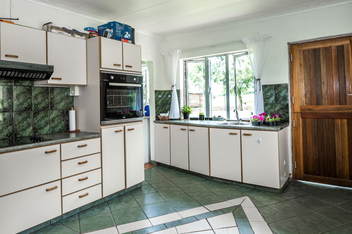 A functional kitchen featuring built-in cabinetry, an integrated oven, extractor fan, and tiled splashbacks with a view of the farm exterior.