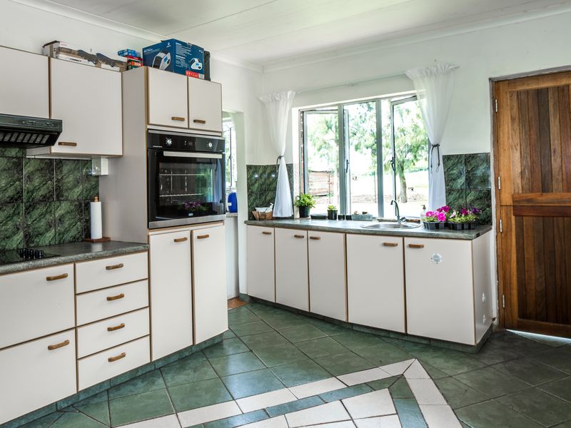 A functional kitchen featuring built-in cabinetry, an integrated oven, extractor fan, and tiled splashbacks with a view of the farm exterior.
