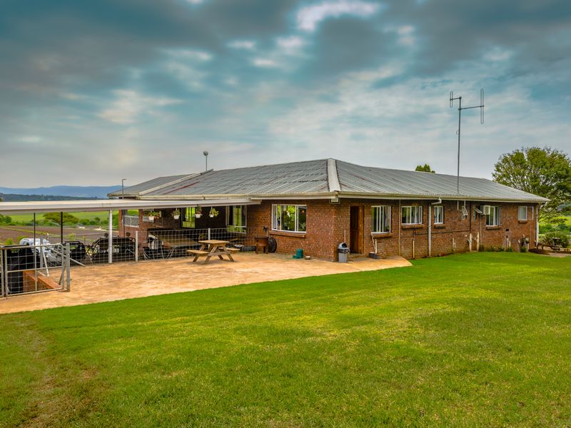 Rear view of a brick farmhouse featuring a corrugated metal roof, a covered patio area, and expansive surrounding lawn.