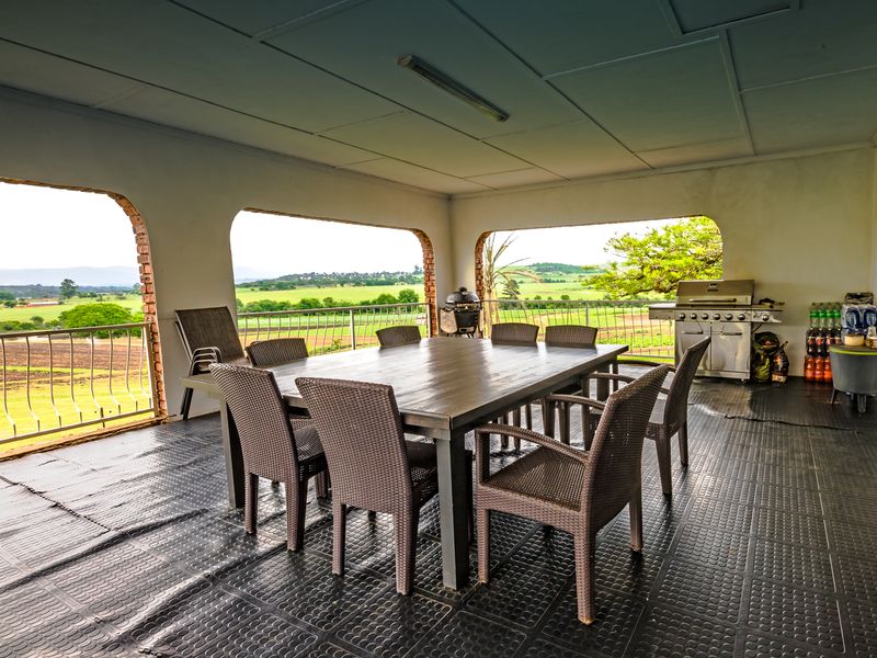 Spacious covered patio featuring a metal balustrade, rubberized flooring, and expansive views of the surrounding farmland, ideal for outdoor dining and entertaining.