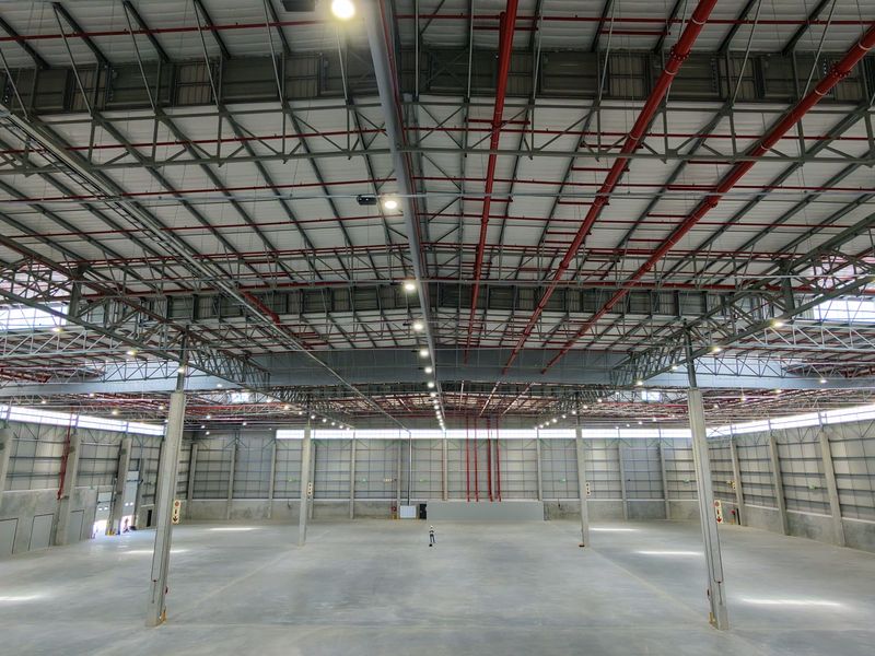 Spacious industrial warehouse featuring high ceilings with exposed steel trusses, fire sprinkler systems, concrete flooring, and ample natural light through clerestory windows.