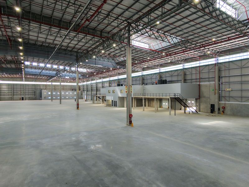 Expansive industrial warehouse space featuring high ceilings with exposed steel trusses, a mezzanine level, concrete flooring, and integrated fire sprinkler systems.