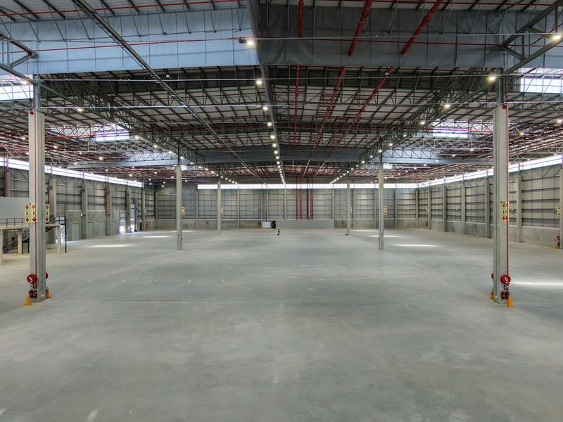 Expansive industrial warehouse space featuring high ceilings, exposed steel trusses, fire sprinkler systems, and a mezzanine level, ideal for logistics or manufacturing operations.