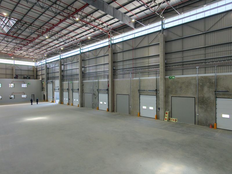 Spacious industrial warehouse featuring high ceilings, exposed steel trusses, multiple roller shutter doors, and polished concrete flooring, suitable for logistics or manufacturing operations.