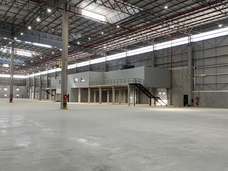 Expansive industrial warehouse space featuring high ceilings, concrete flooring, a mezzanine level with staircase access, and integrated fire safety systems.