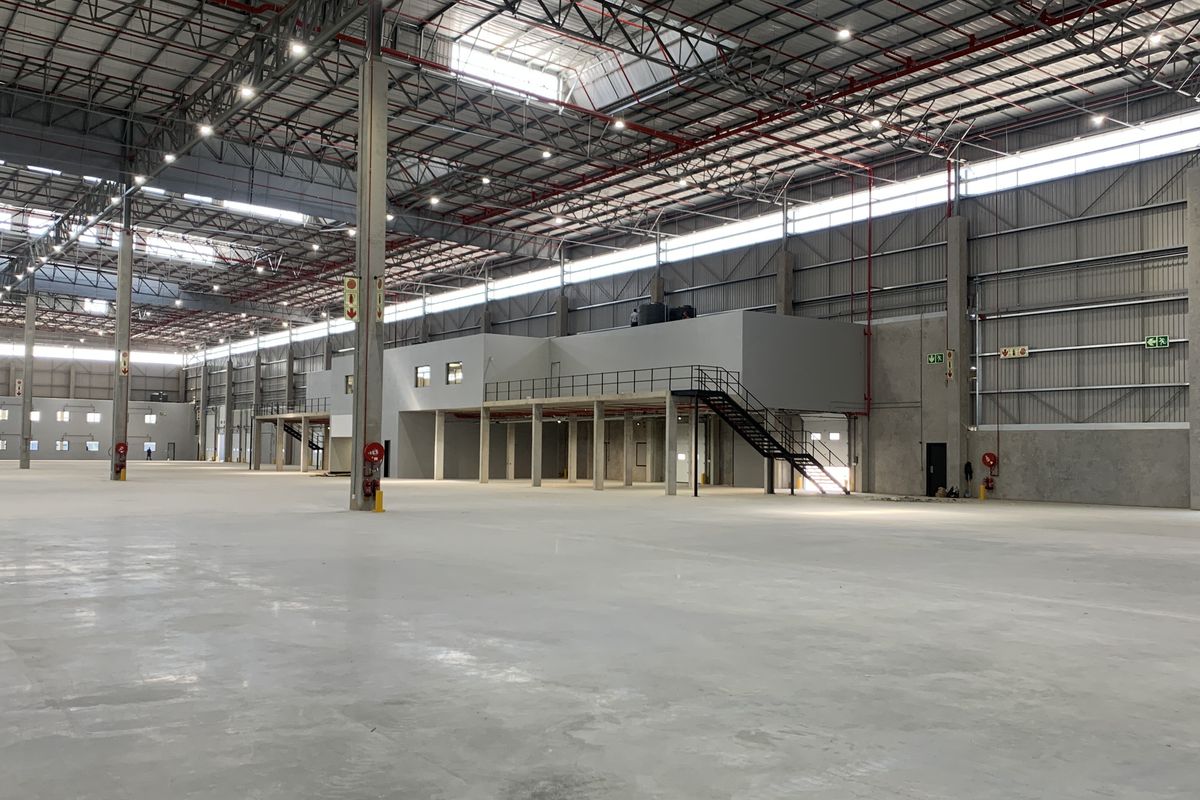 Expansive industrial warehouse space featuring high ceilings, concrete flooring, a mezzanine level with staircase access, and integrated fire safety systems.