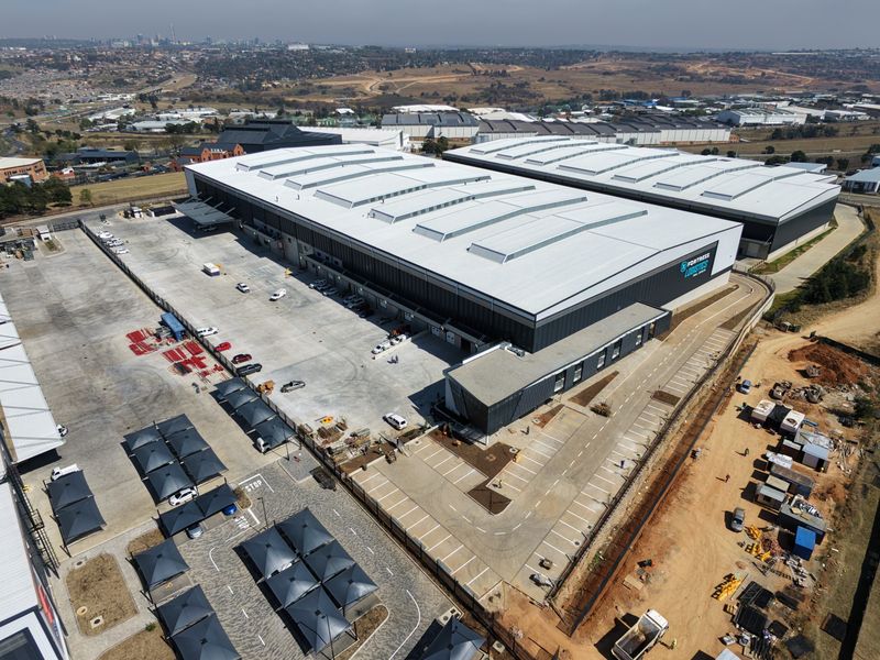 Aerial view of a modern industrial logistics facility featuring a large warehouse, extensive concrete yard, loading docks, and dedicated covered parking areas.