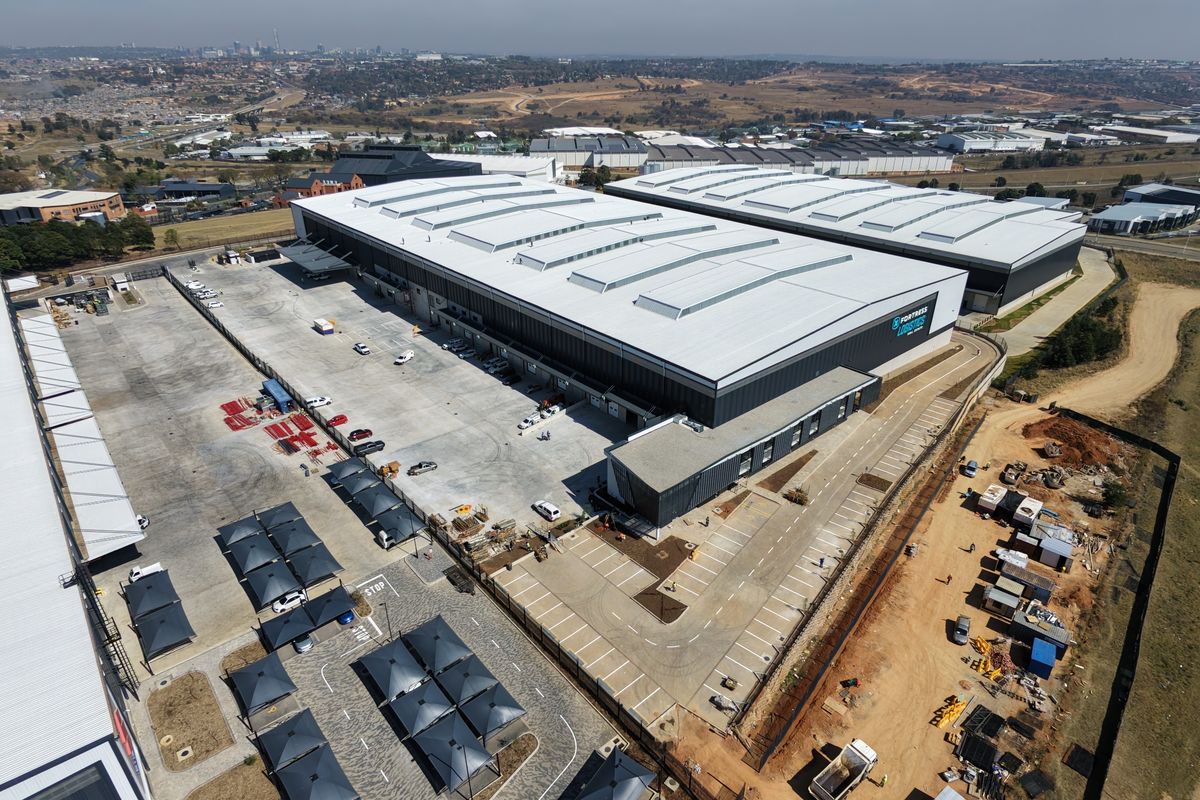 Aerial view of a modern industrial logistics facility featuring a large warehouse, extensive concrete yard, loading docks, and dedicated covered parking areas.