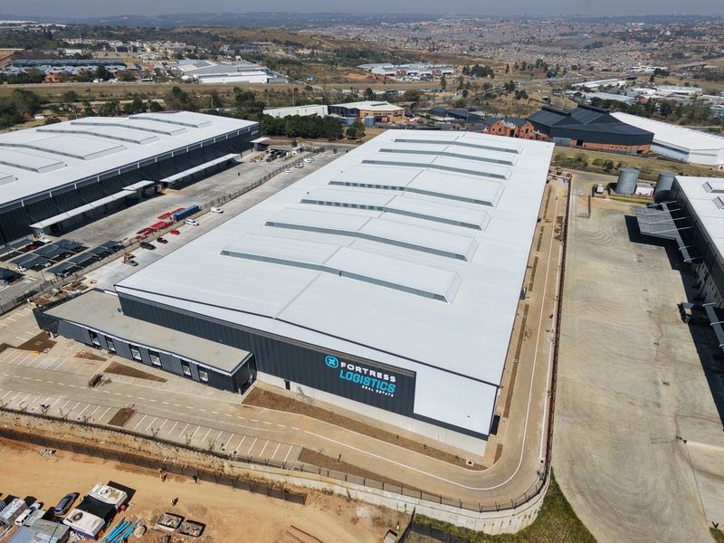 Aerial view of a modern industrial logistics warehouse facility featuring extensive roof skylights, paved yard space, and secure perimeter fencing.
