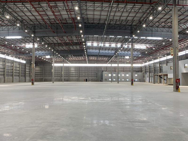 A large, open-plan industrial warehouse space featuring polished concrete floors, high-clearance steel truss ceilings, and integrated fire safety systems.