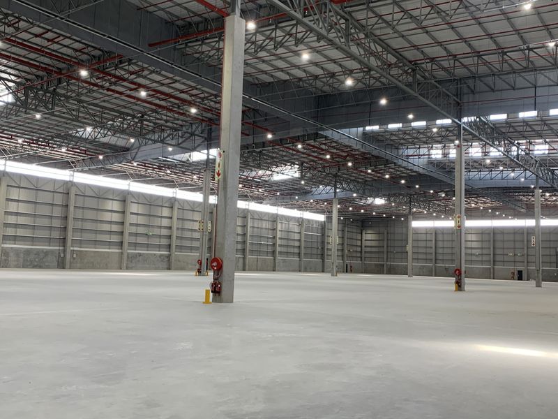 Expansive industrial warehouse space featuring high ceilings, exposed steel truss roofing, polished concrete flooring, and integrated fire safety systems.
