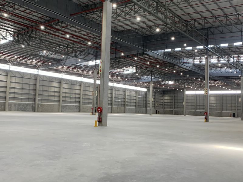 A large, modern industrial warehouse space featuring high ceilings, concrete flooring, exposed steel trusses, and integrated fire sprinkler systems.