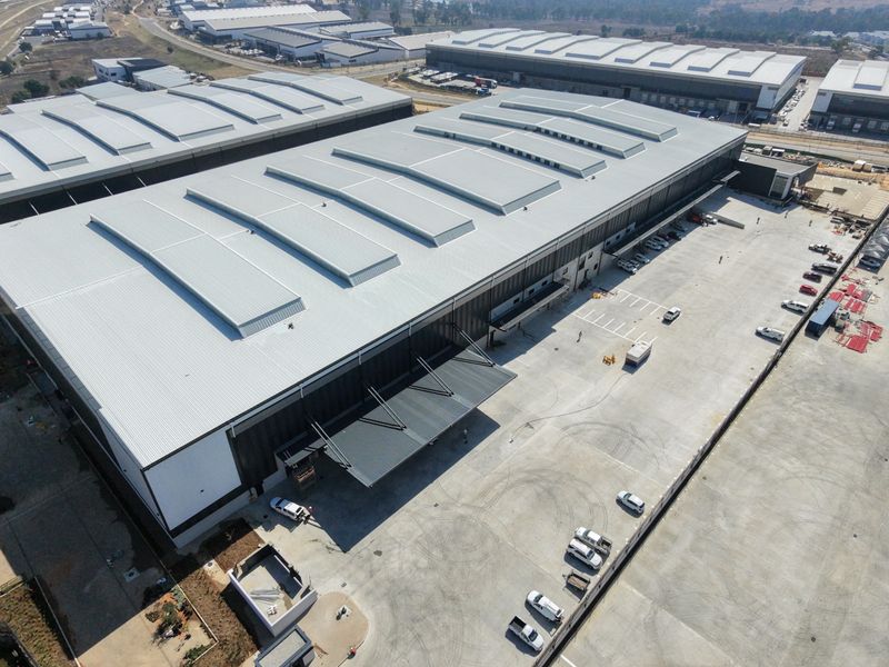 Aerial view of a large industrial warehouse facility featuring a metal roof with skylights, a loading canopy, and an expansive concrete yard.