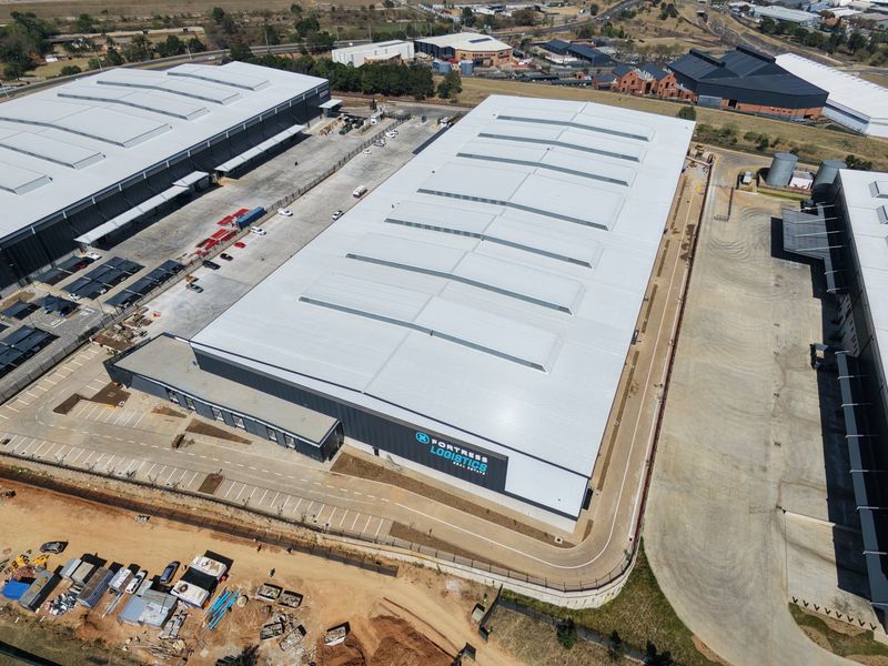 Aerial view of a large industrial warehouse facility featuring a metal roof, skylights, and extensive paved parking and driveway areas.