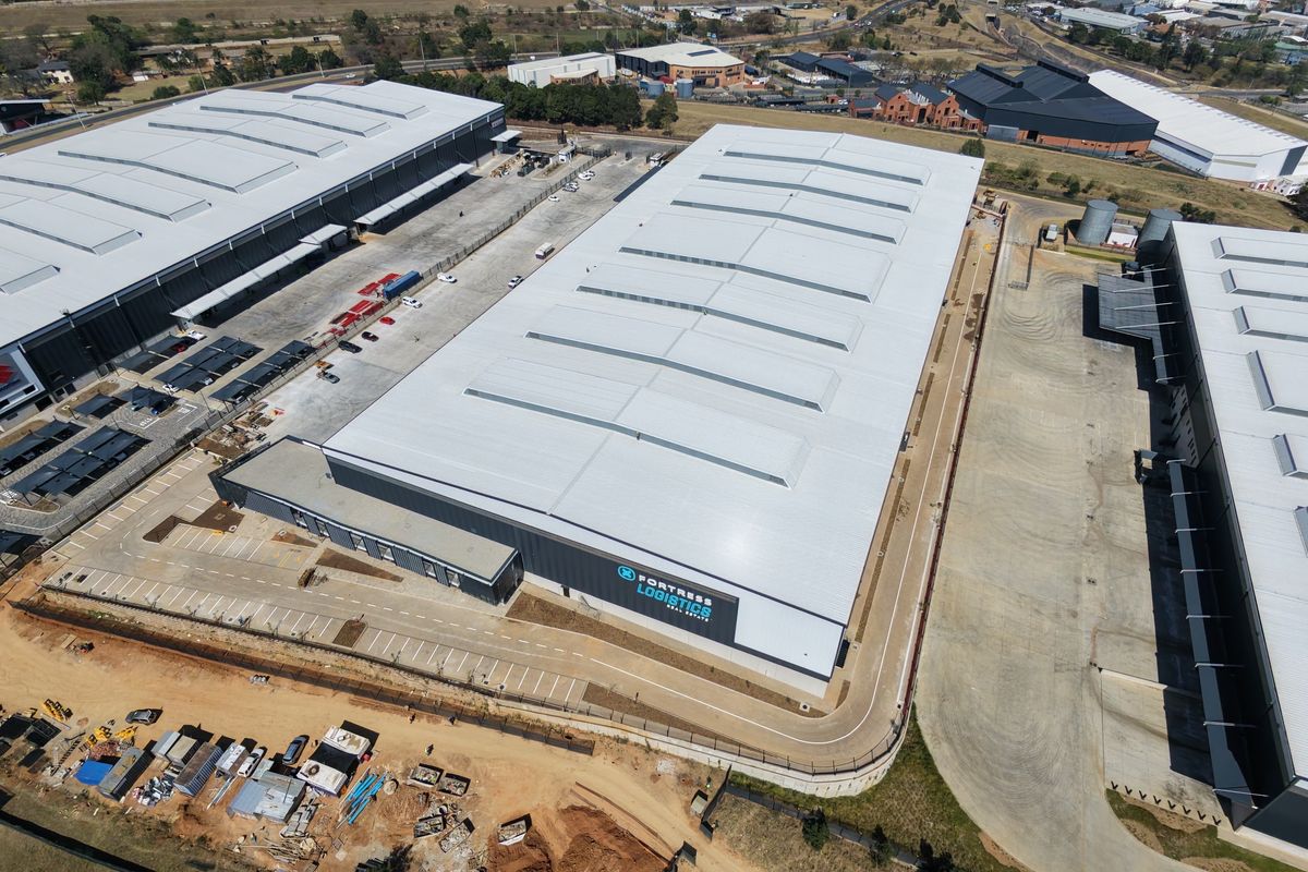 Aerial view of a large industrial warehouse facility featuring a metal roof, skylights, and extensive paved parking and driveway areas.