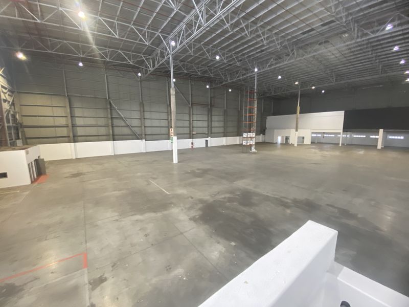 Spacious industrial warehouse featuring high ceilings with exposed steel trusses, polished concrete flooring, and high-bay lighting, suitable for storage or manufacturing operations.