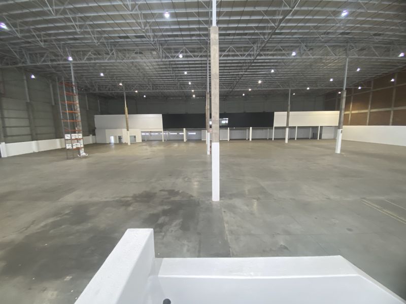 Expansive industrial warehouse space featuring high ceilings, exposed steel trusses, high bay lighting, and durable concrete flooring, suitable for logistics or manufacturing operations.