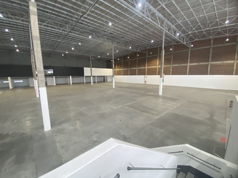 A spacious, open-plan industrial warehouse featuring high ceilings with exposed steel trusses, concrete flooring, and ample natural light, suitable for various commercial operations.