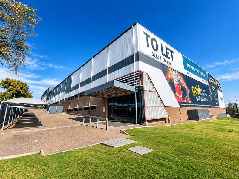 Modern industrial warehouse facility featuring a large facade, paved parking area with shade structures, and prominent signage for lease.