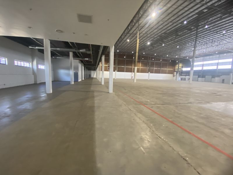 Expansive industrial warehouse space featuring high ceilings with exposed steel trusses, concrete flooring, and ample support columns, suitable for storage or manufacturing operations.