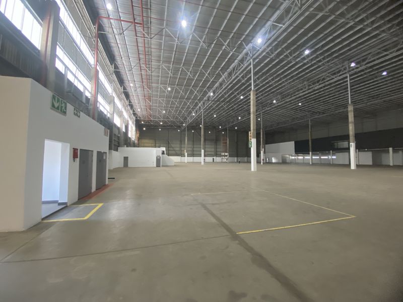 Spacious industrial warehouse featuring high ceilings with exposed steel trusses, polished concrete flooring, fire sprinkler systems, and integrated internal office facilities.