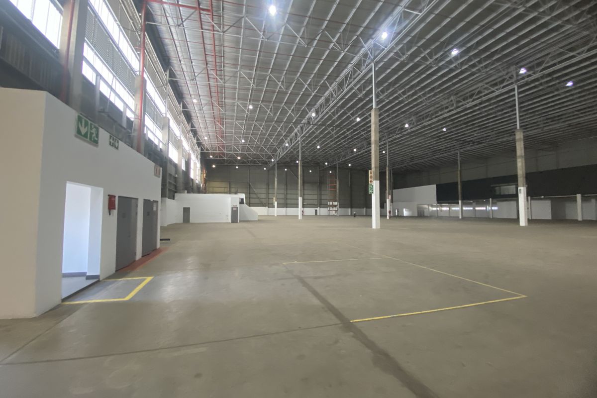 Spacious industrial warehouse featuring high ceilings with exposed steel trusses, polished concrete flooring, fire sprinkler systems, and integrated internal office facilities.