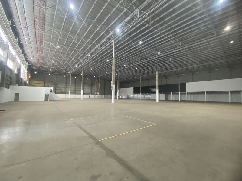 Expansive industrial warehouse space featuring high ceilings, exposed steel roof trusses, polished concrete flooring, and integrated high-bay lighting systems.