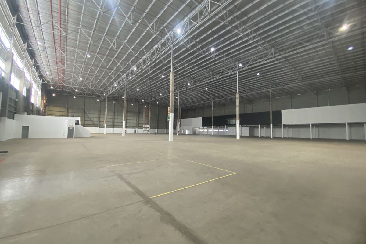 Expansive industrial warehouse space featuring high ceilings, exposed steel roof trusses, polished concrete flooring, and integrated high-bay lighting systems.