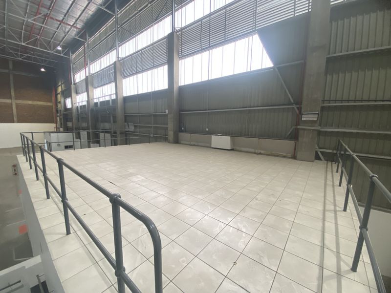 Spacious industrial mezzanine level featuring tiled flooring, metal safety railings, and high-volume ceilings with exposed structural steel and natural light.