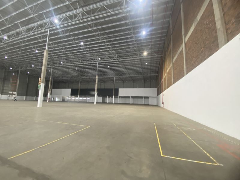Spacious industrial warehouse featuring high ceilings with exposed steel trusses, concrete flooring, and a combination of brick and painted wall finishes.