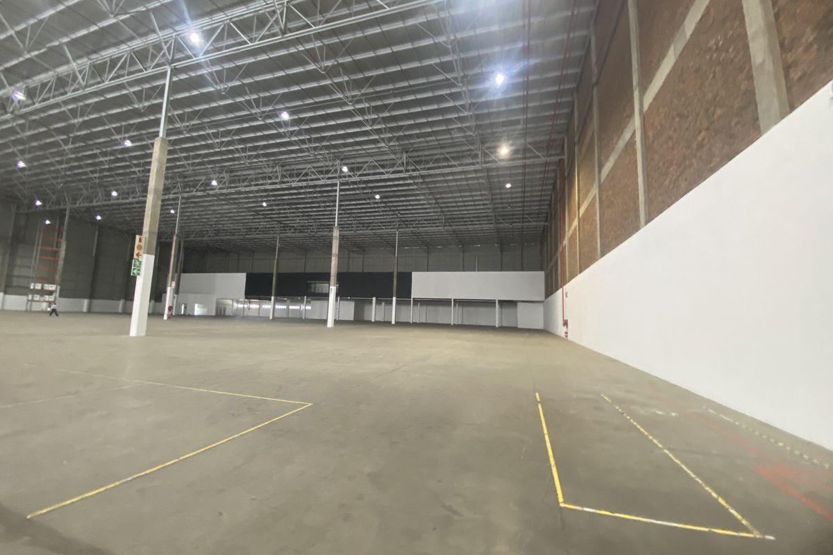 Spacious industrial warehouse featuring high ceilings with exposed steel trusses, concrete flooring, and a combination of brick and painted wall finishes.