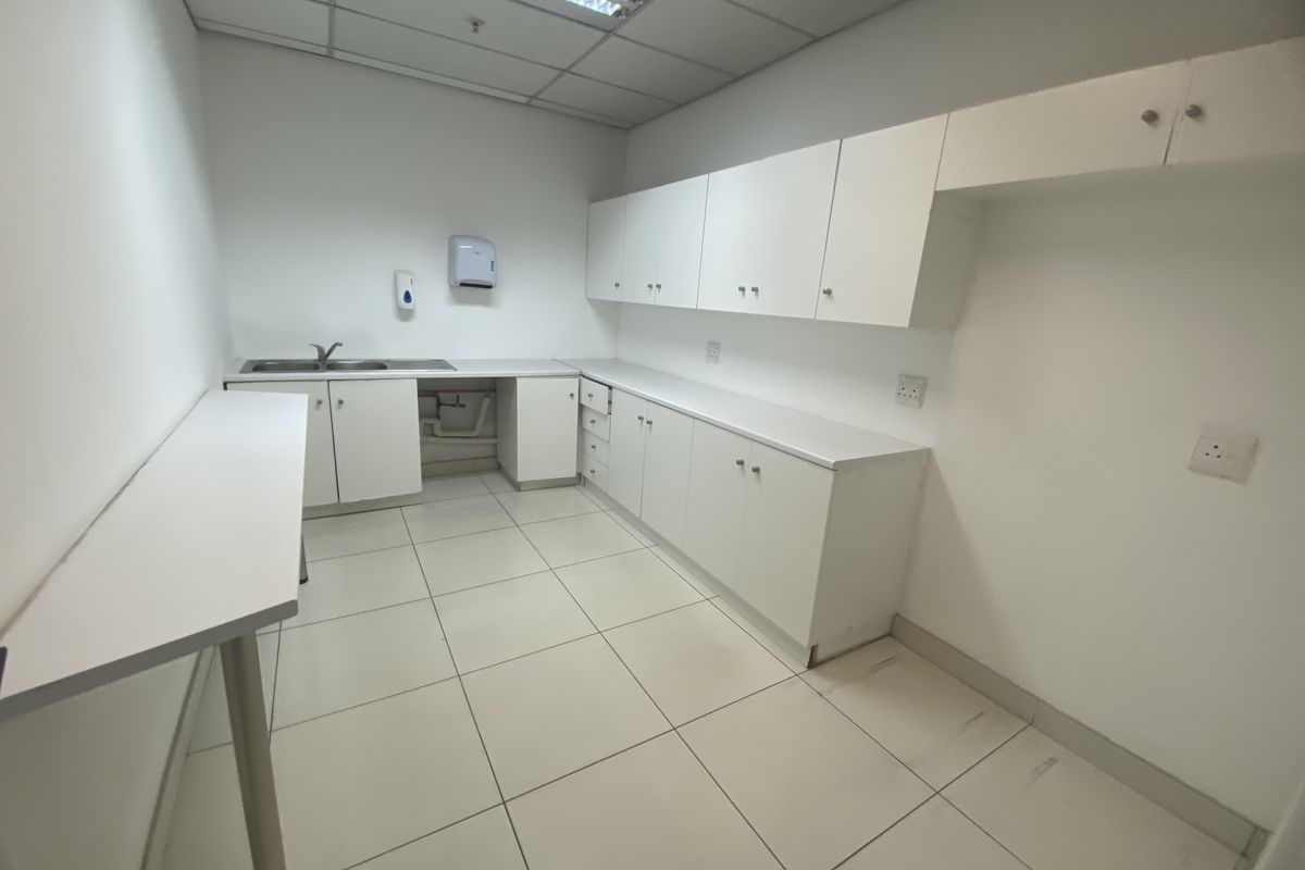 A clean, functional industrial kitchenette featuring white built-in cabinetry, a stainless steel sink, and durable ceramic floor tiles.