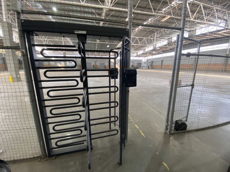 Industrial warehouse interior featuring a secure turnstile access point with integrated electronic security reader, high ceilings, and open concrete floor space.