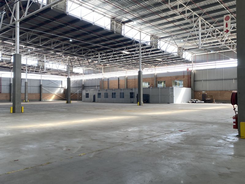 Spacious industrial warehouse featuring high-clearance steel truss roofing, polished concrete flooring, integrated office block, and natural light through overhead skylights.